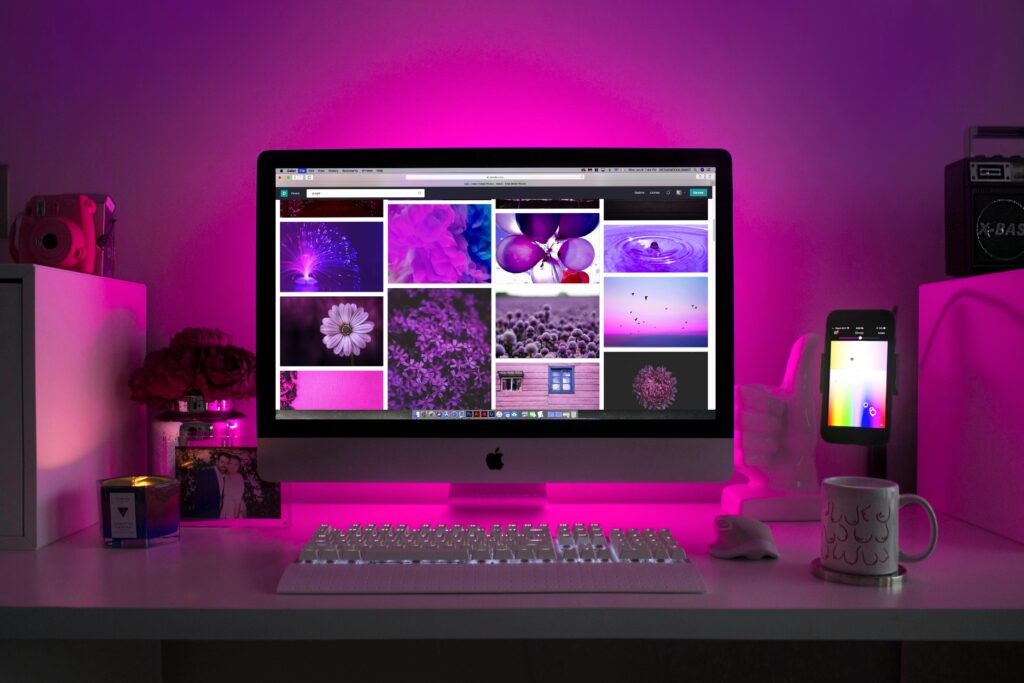 Modern desk setup with neon lighting and a desktop computer displaying colorful images.