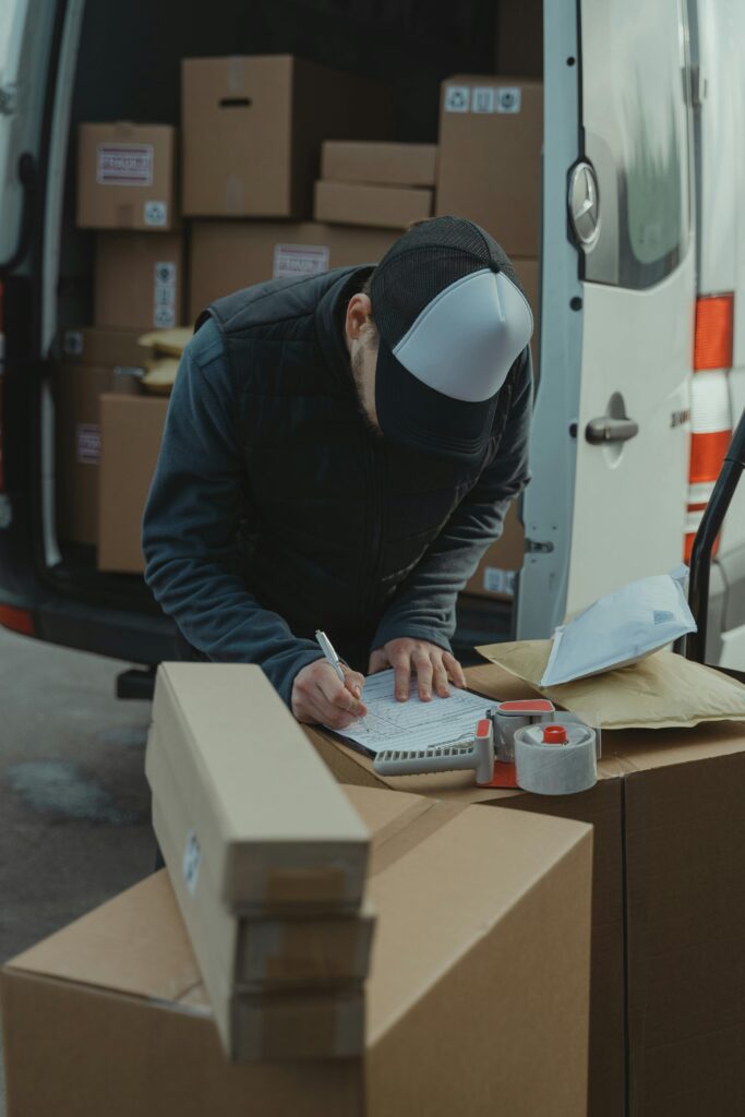 Courier organizing packages from a van, preparing for delivery in a logistics setting.